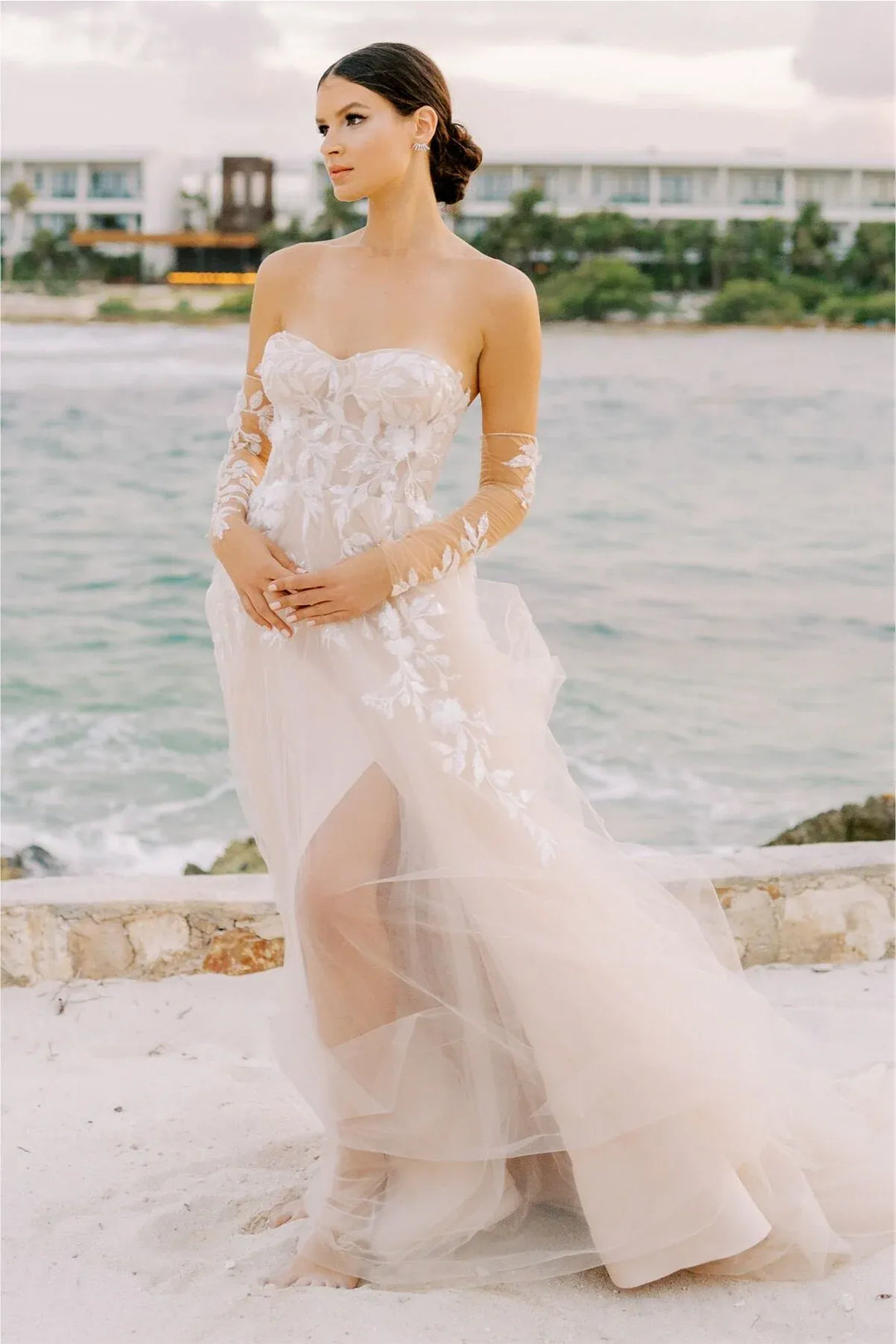Woman in a white wedding dress standing on a beach with ocean and sky in the background