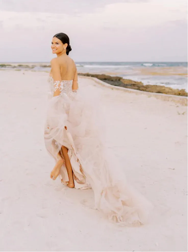 Woman in a flowing dress on a sandy beach with ocean and sky in the background