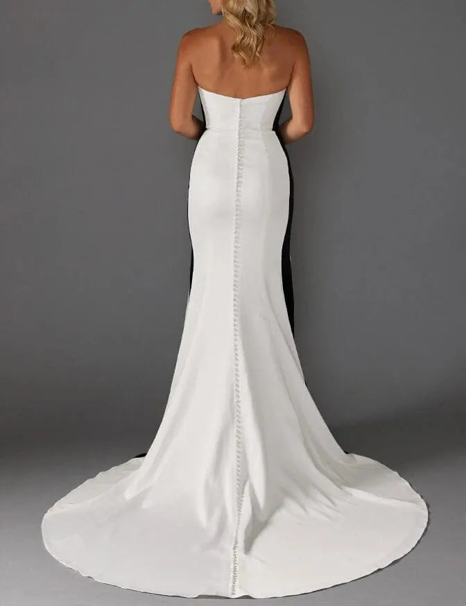 A strapless white mermaid-style wedding dress shown from the back, featuring a fitted bodice, a long center backline with bead detailing, and a full train against a dark gray studio background.