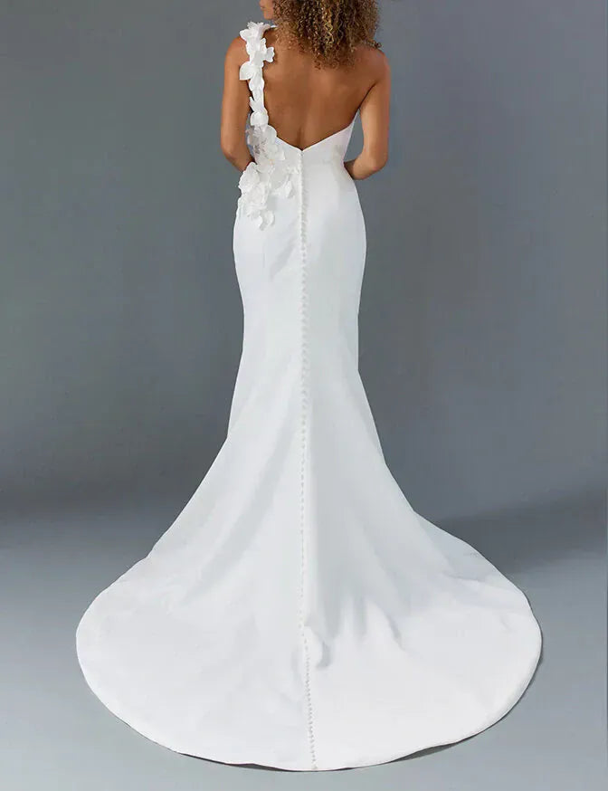 back of louvienne enzo ivory crepe fitted wedding dress with a one shoulder neckline with dimensional floral accents, and a chapel length train