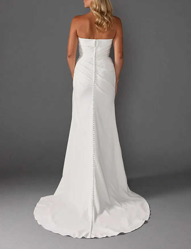 A strapless white wedding gown shown from the back, featuring a structured bodice, a central back zipper with decorative studs, and a slight train, worn by a model against a dark gray studio background.