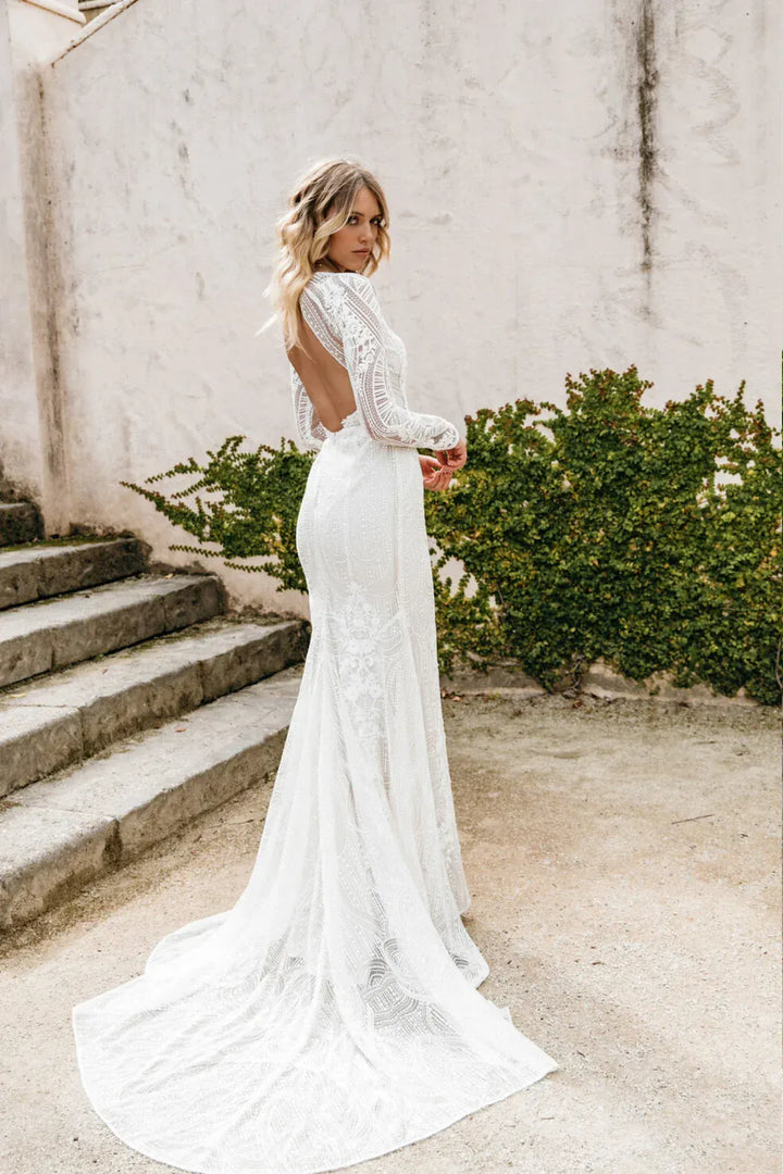 Woman in a white lace wedding dress standing outdoors with a neutral background