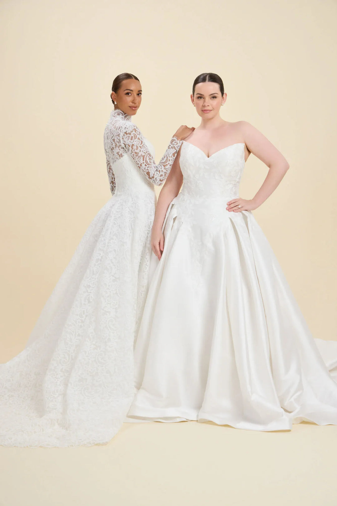 Two models wearing white wedding dresses against a warm beige studio background. The model on the left wears a long-sleeve lace wedding gown with a high neck and full skirt, while the model on the right wears a strapless white satin ball gown with a sweetheart neckline and full skirt.