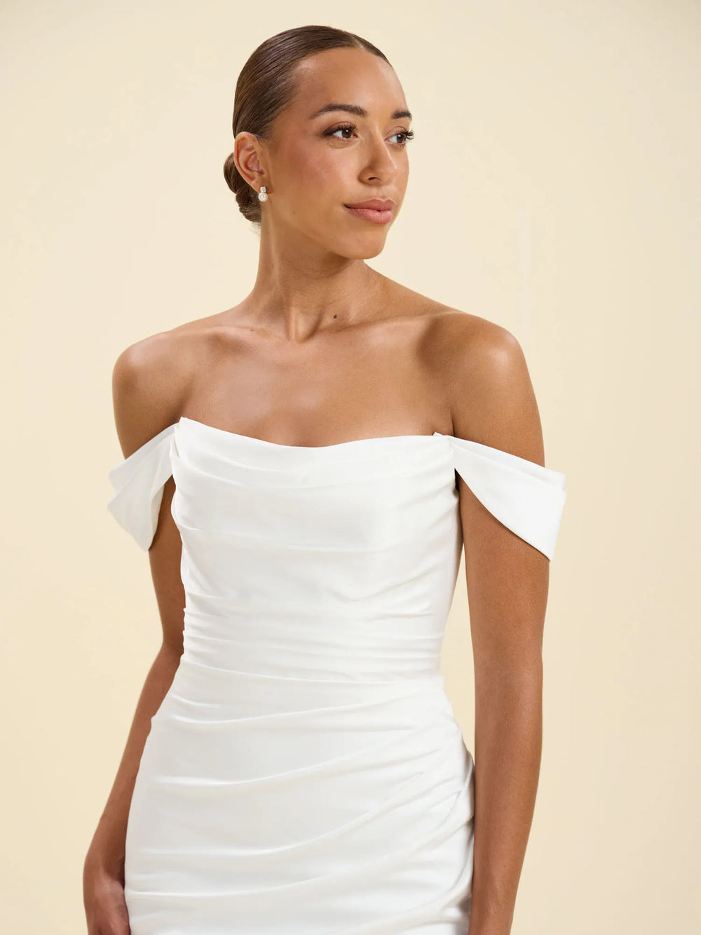 A woman wearing a white off-the-shoulder ruched dress, photographed against a solid light beige studio background.