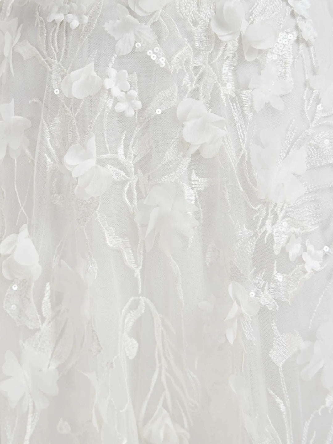 Close-up of a white floral lace fabric with 3D floral appliqués, embroidered vines, and small sequins.