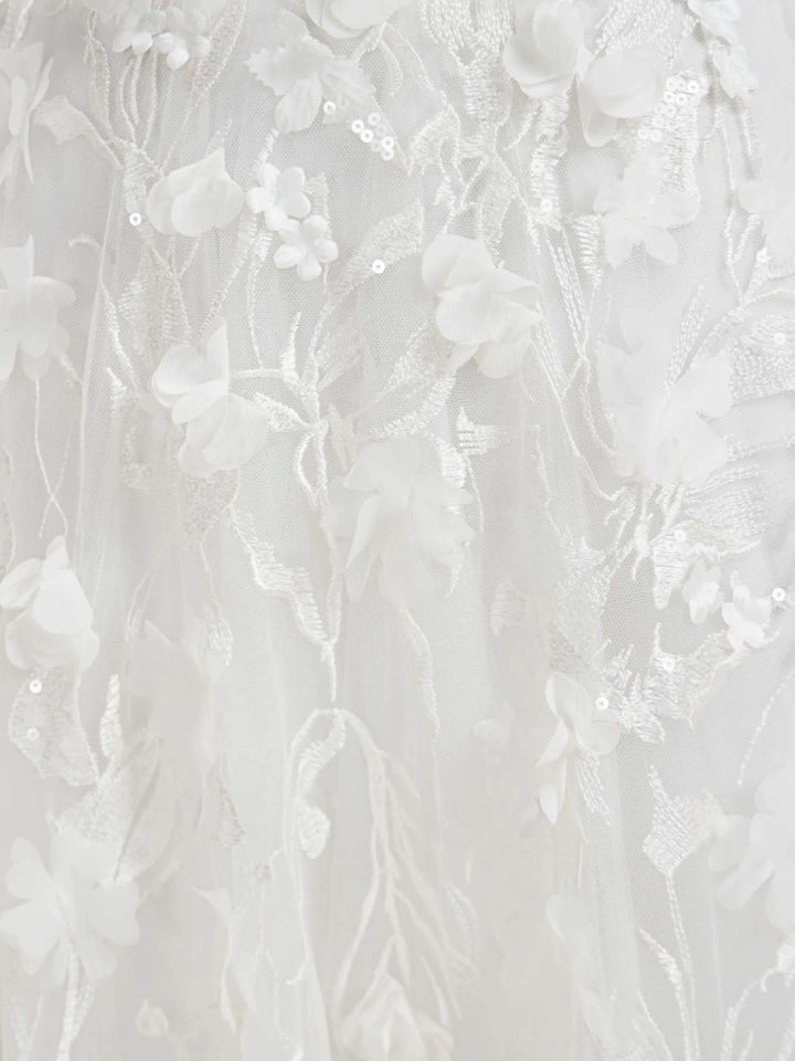 Close-up of a white floral lace fabric with 3D floral appliqués, embroidered vines, and small sequins.