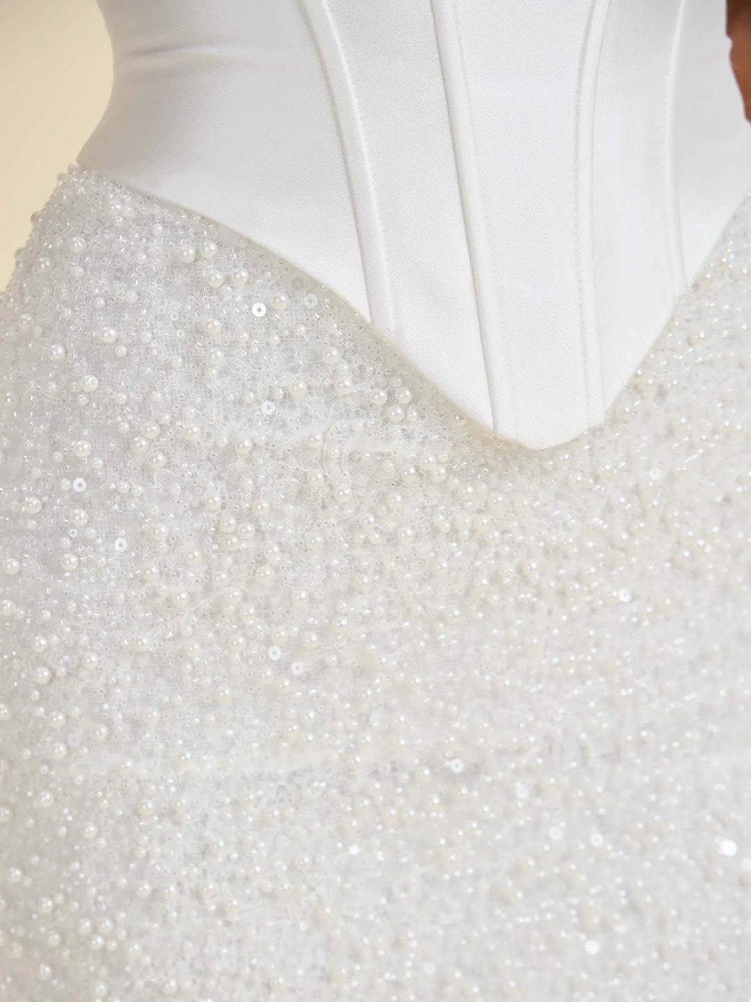 Close-up of a white bridal gown with a structured corset-style bodice and dense pearl and bead embellishment across the skirt.