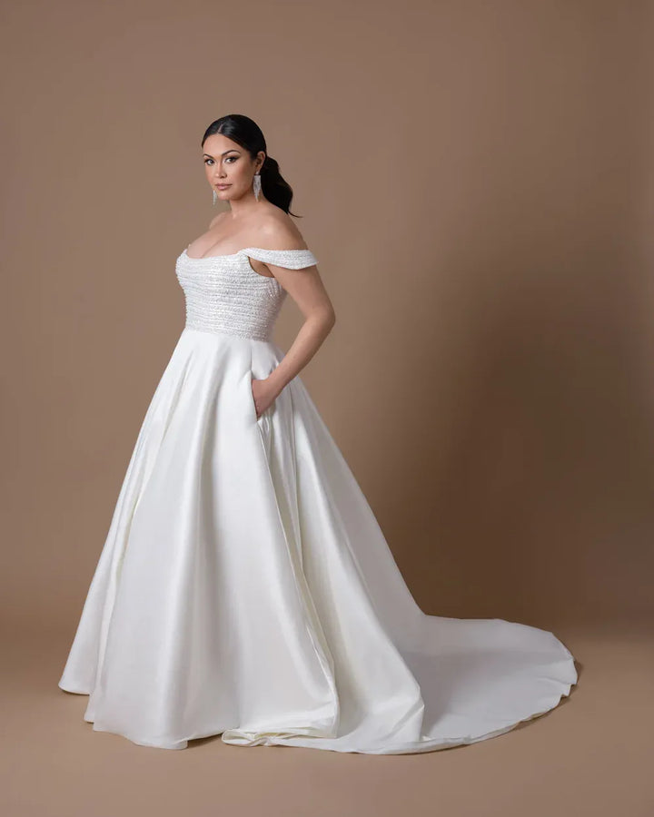 side of dany girl luxe ivory satin ball gown wedding dress with a beaded scoop neck bodice, and pockets in the skirt