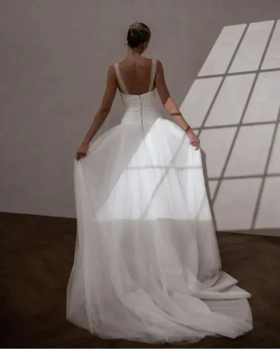 Woman in a white wedding dress with a long train, standing in a room with geometric wall design.