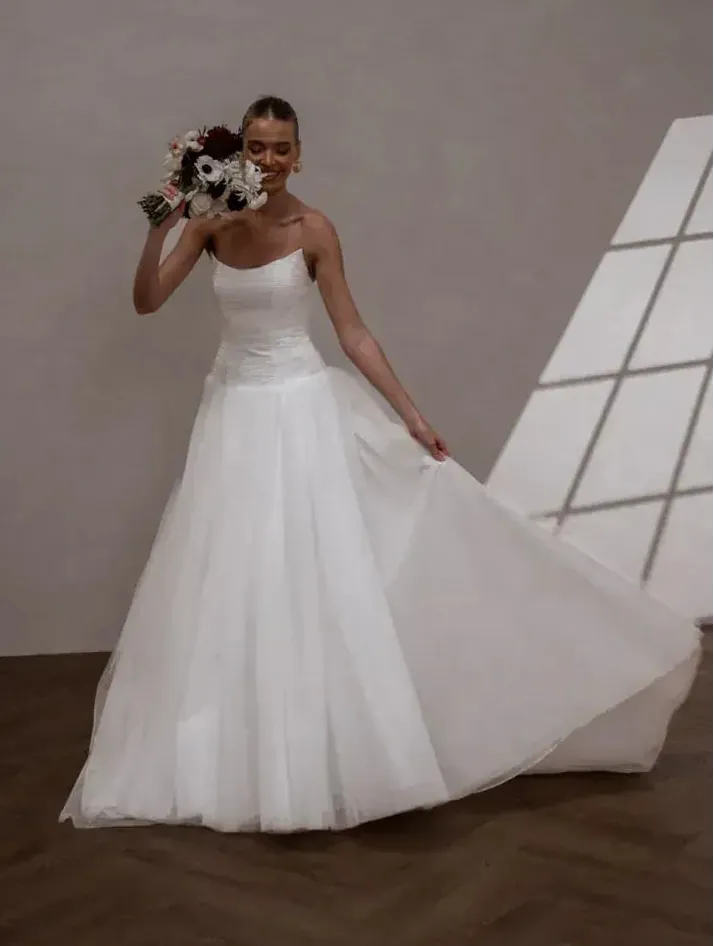 Woman in a white wedding dress holding flowers against a neutral background
