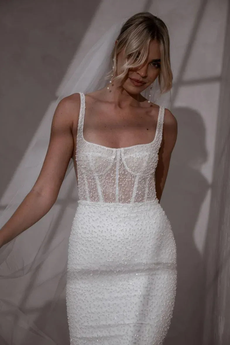 close up of the front of made with love freddie ivory beaded fit and flare wedding dress with a square neckline and fitted skirt