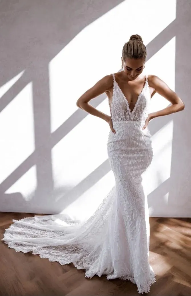 Woman wearing a white lace wedding dress in a bright room with sunlight streaming through.