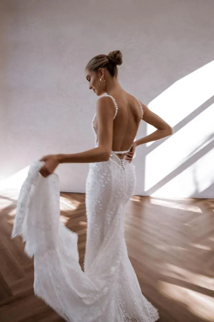 Woman in a white wedding dress with a high slit, standing in a softly lit room.