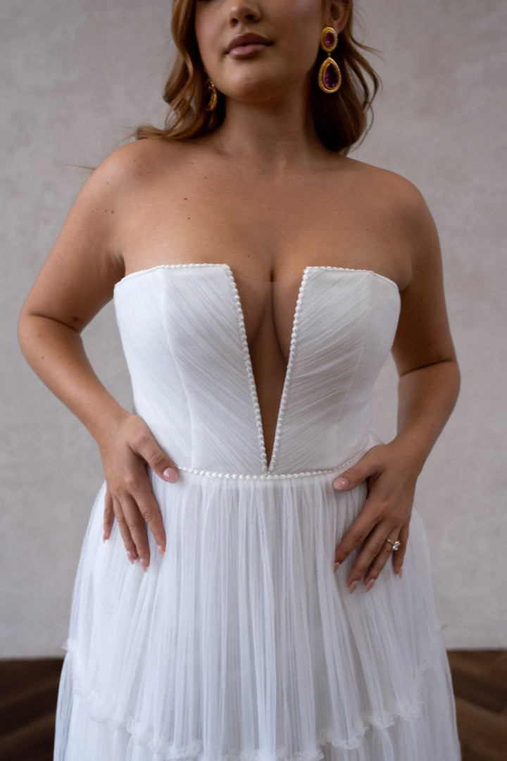 Woman wearing a strapless white dress with a deep neckline against a neutral background