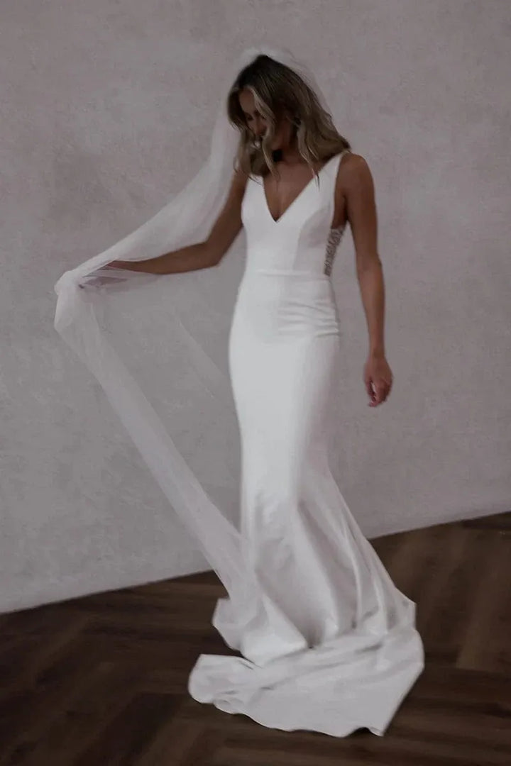 Woman in a white wedding dress with a long veil against a neutral background