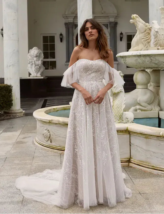 Woman in a strapless lace wedding dress standing in front of classical architecture.