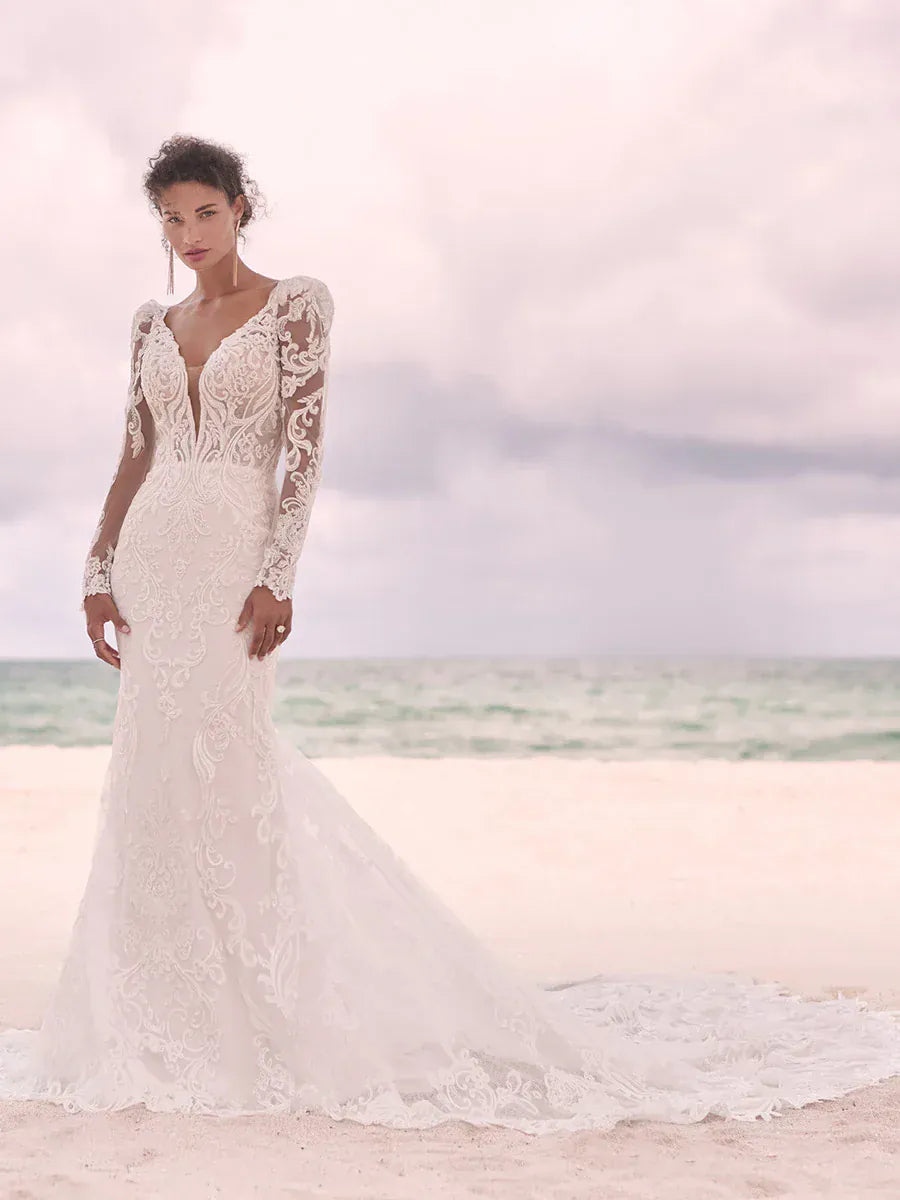 Woman in a lace wedding dress standing on a beach with ocean in the background
