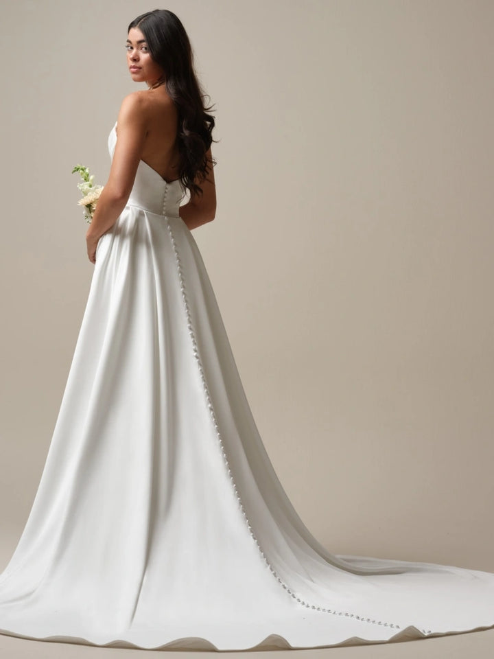 full back of maggie sottero camille ivory satin fitted wedding dress featuring a strapless bodice, showing with the matching overskirt with buttons down the back