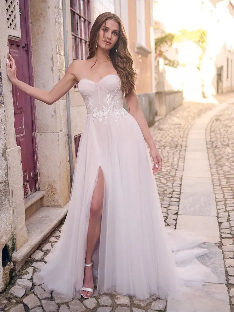 Woman in a white strapless gown with a high slit standing on a cobblestone street.
