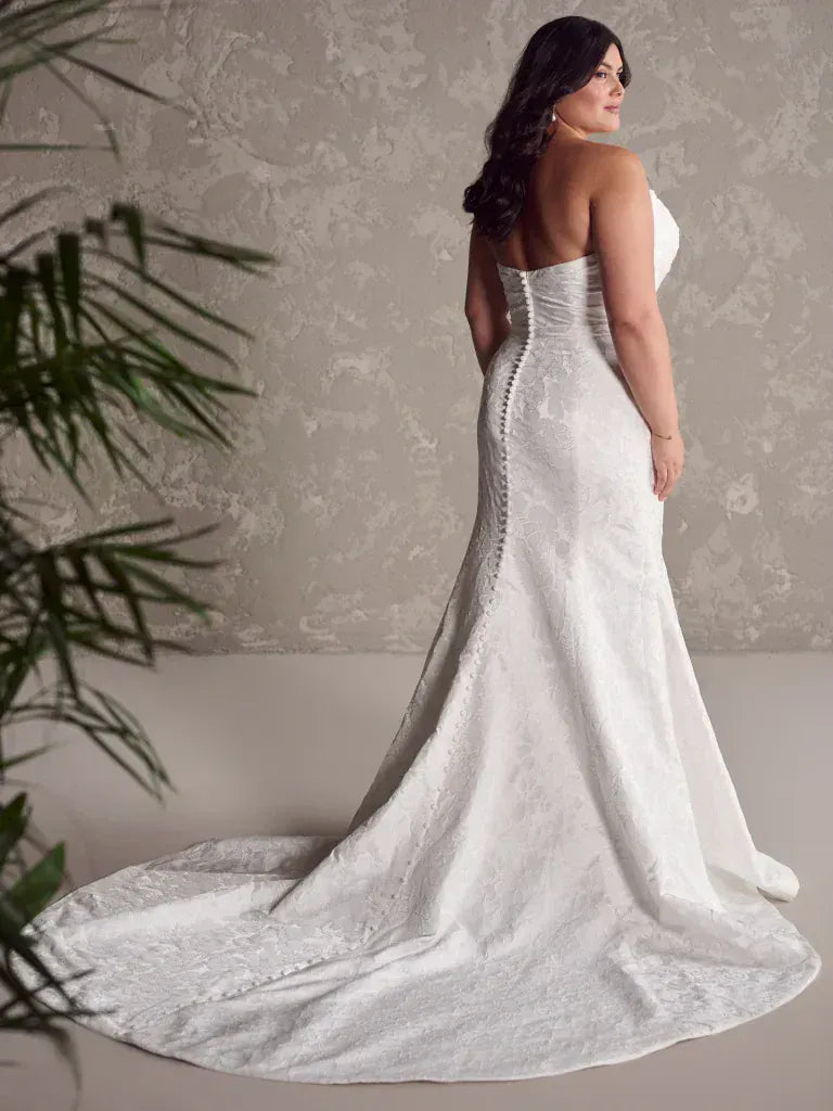 Woman wearing a white wedding dress with a long train against a neutral background