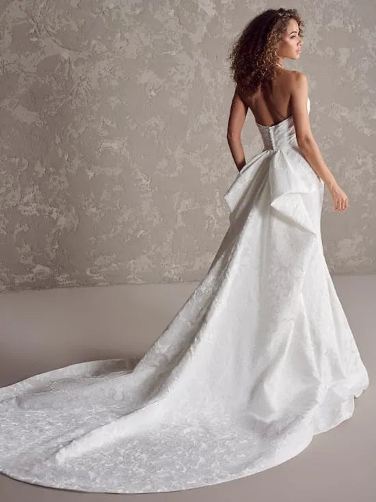Woman wearing a white wedding dress with a long train against a neutral background