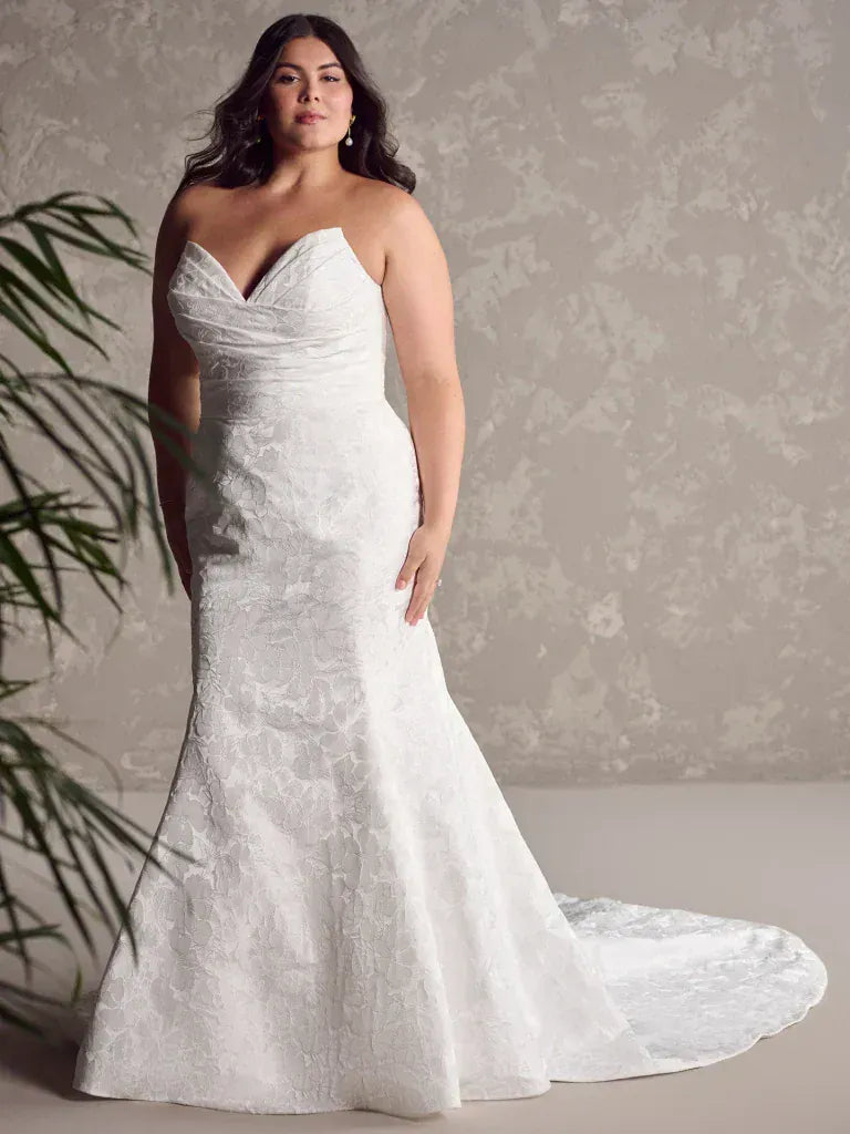 Woman wearing a white strapless wedding dress with a long train against a neutral background
