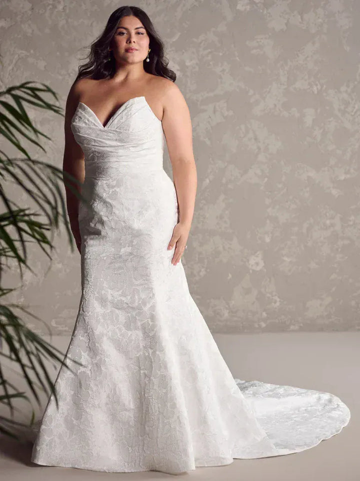 Woman wearing a white strapless wedding dress with a long train against a neutral background
