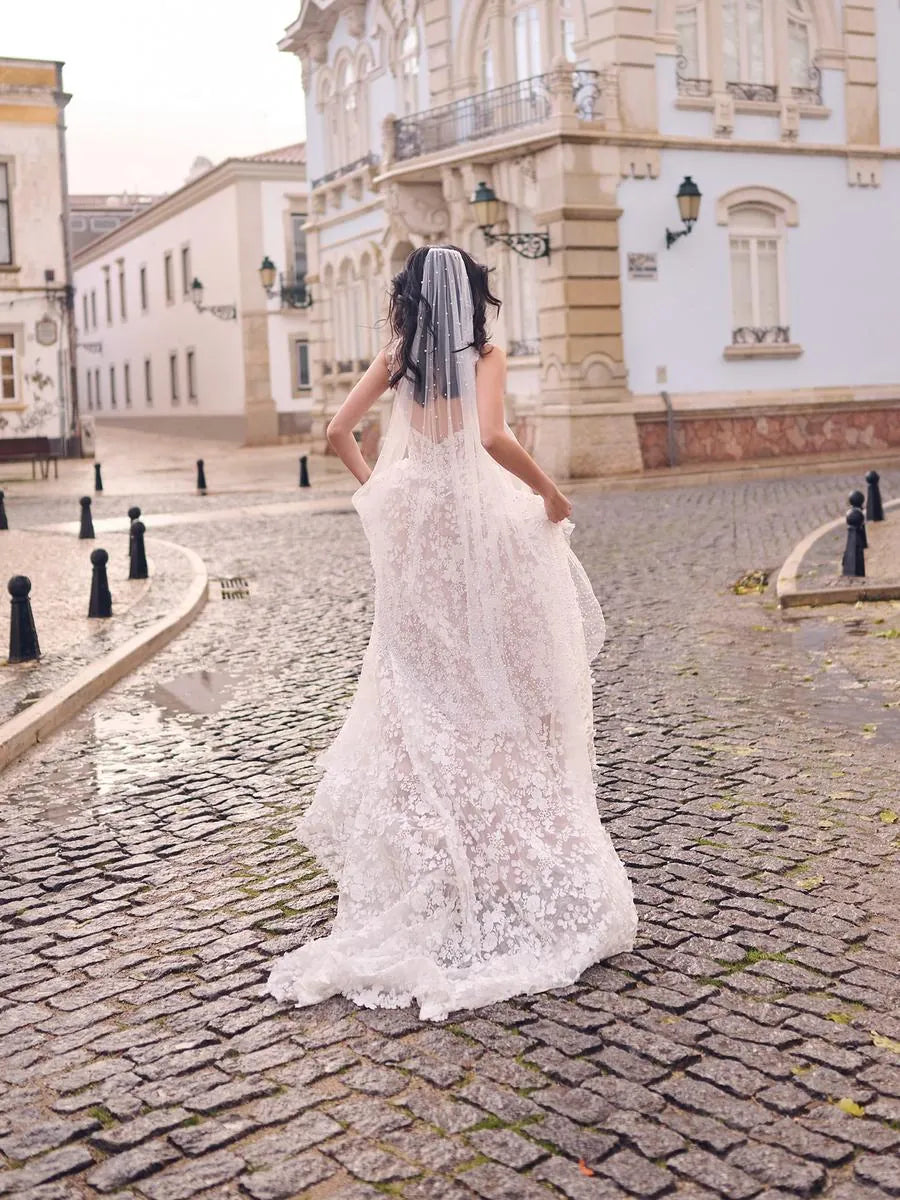 Woman in a white lace wedding dress walking on a cobblestone street.
