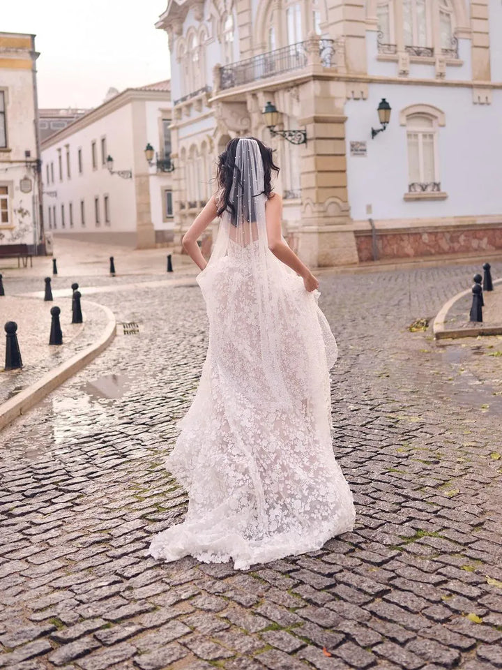Woman in a white lace wedding dress walking on a cobblestone street.