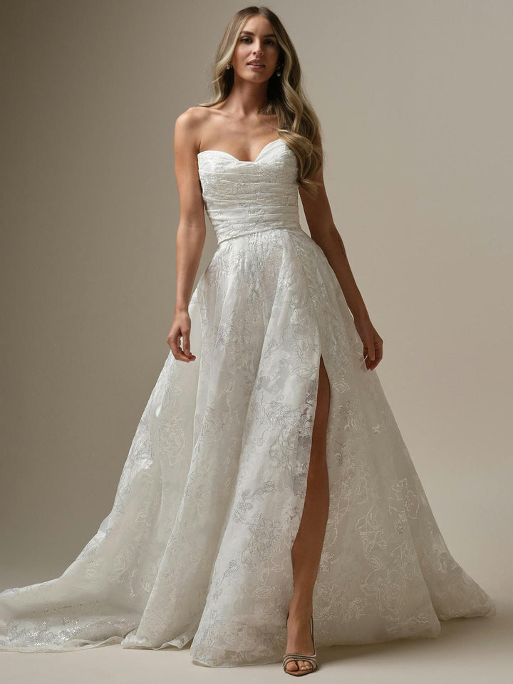Woman wearing a strapless lace wedding dress with a slit on a neutral background