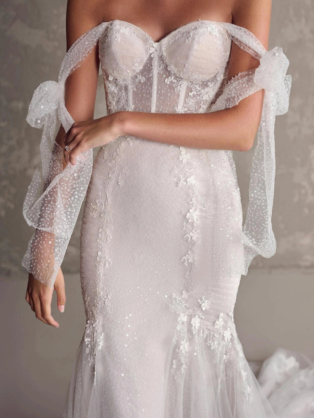 Elegant white wedding dress with sheer sleeves and intricate detailing on a neutral background