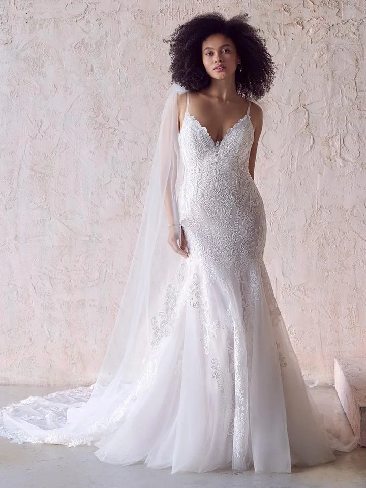 Woman wearing a white lace wedding dress with a flowing train against a light background