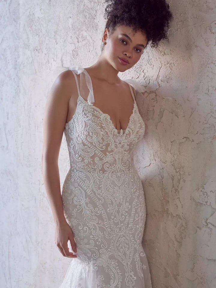 Woman wearing a lace wedding dress against a textured wall.