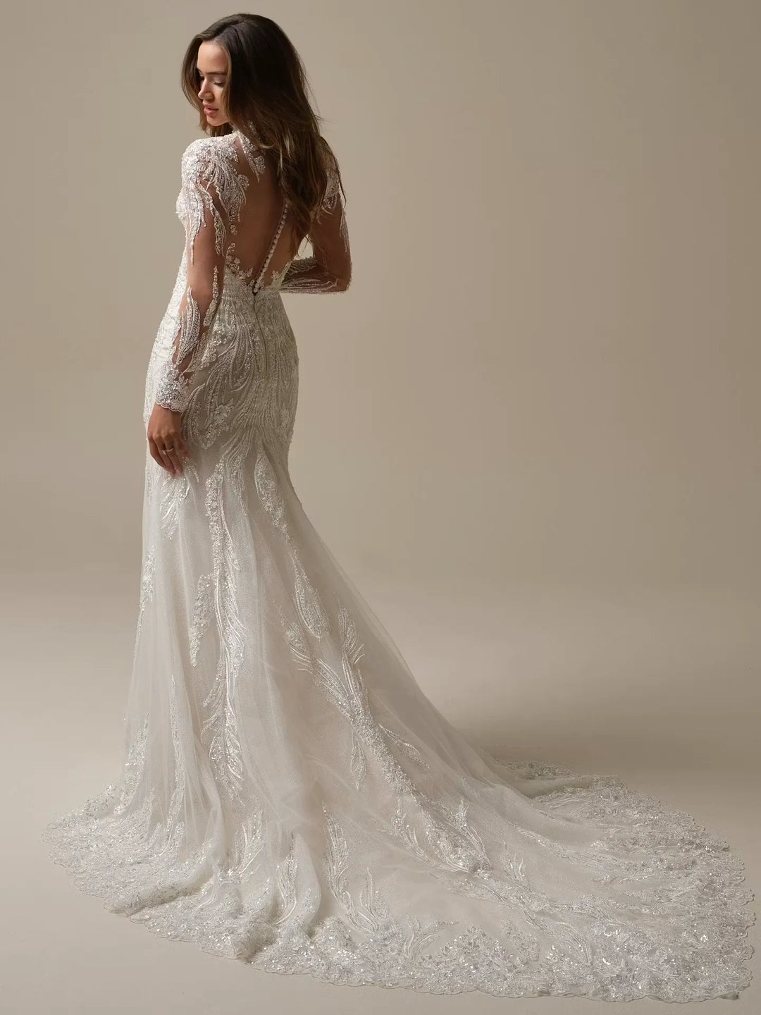 Woman wearing a lace wedding dress with a long train on a plain background