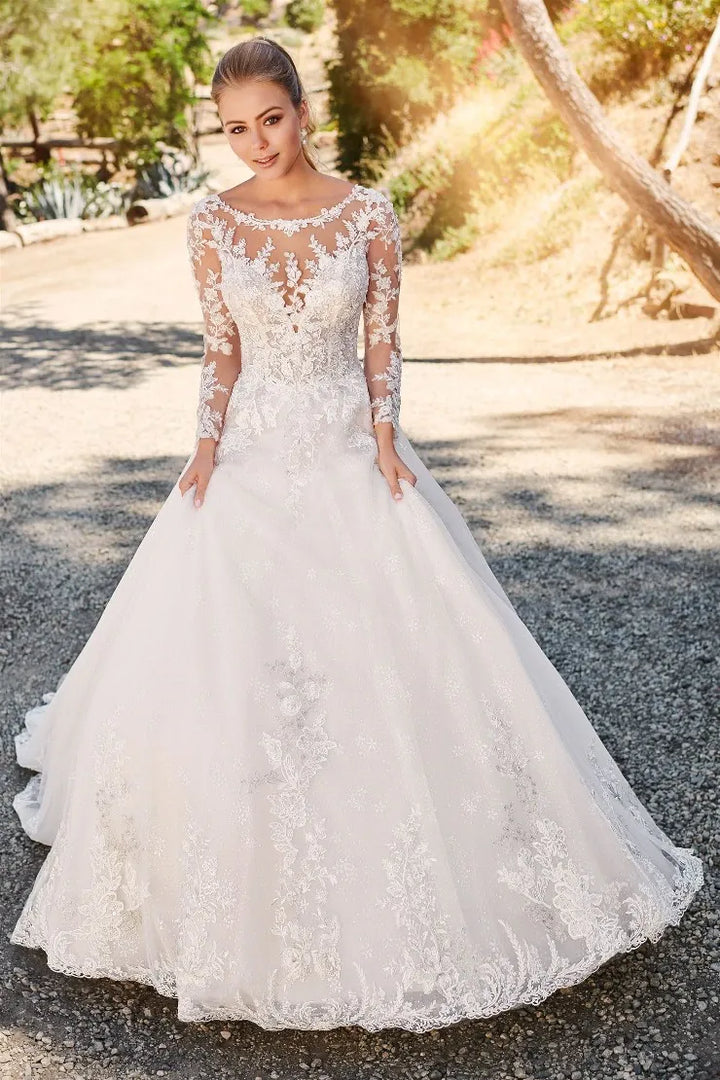 Woman in a white lace wedding dress standing outdoors with trees in the background