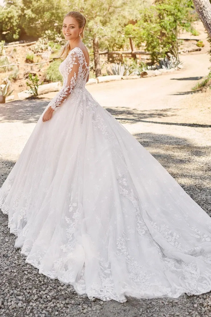 Woman in a white lace wedding dress standing outdoors with greenery in the background