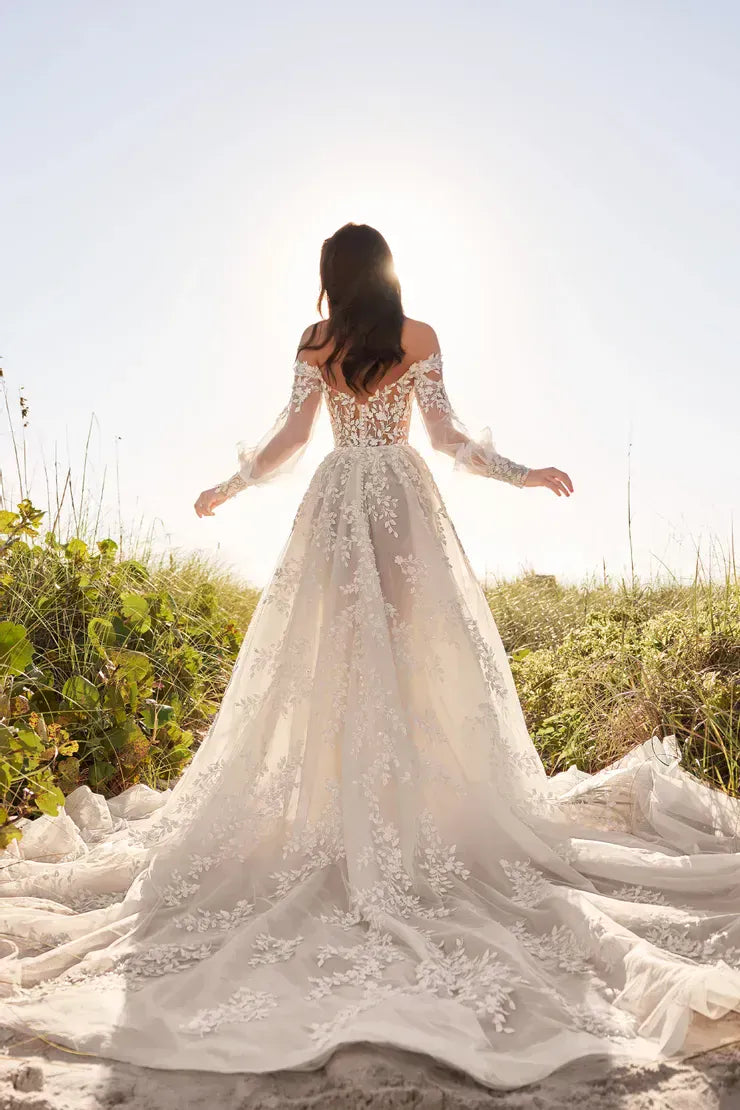 Woman in a white wedding dress standing on a beach with greenery around.