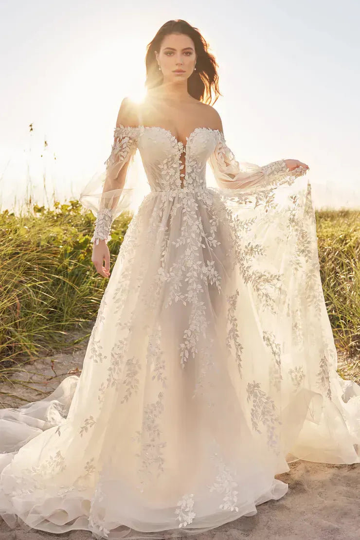 Woman in a white wedding dress with floral details standing on a beach.