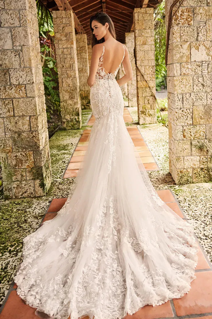 Woman in a white lace wedding dress standing in a tropical setting with stone columns.