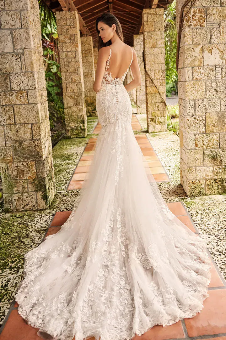 Woman in a white lace wedding dress standing in a tropical setting with stone columns.