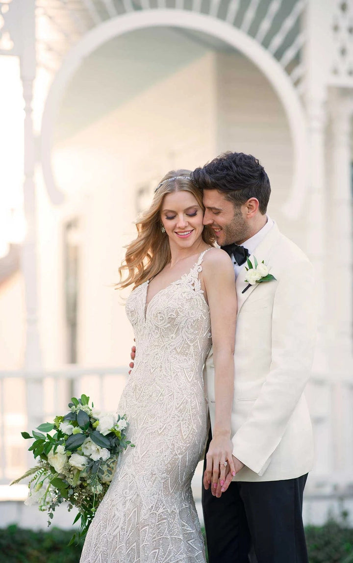 Couple in wedding attire standing close together with a decorative archway in the background.