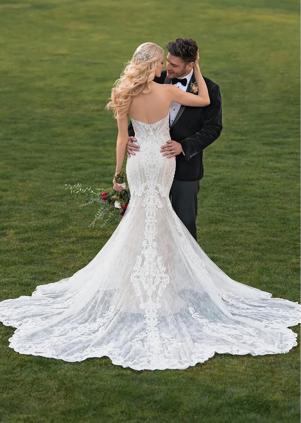 Man embracing a woman in a white wedding dress on a grassy field.