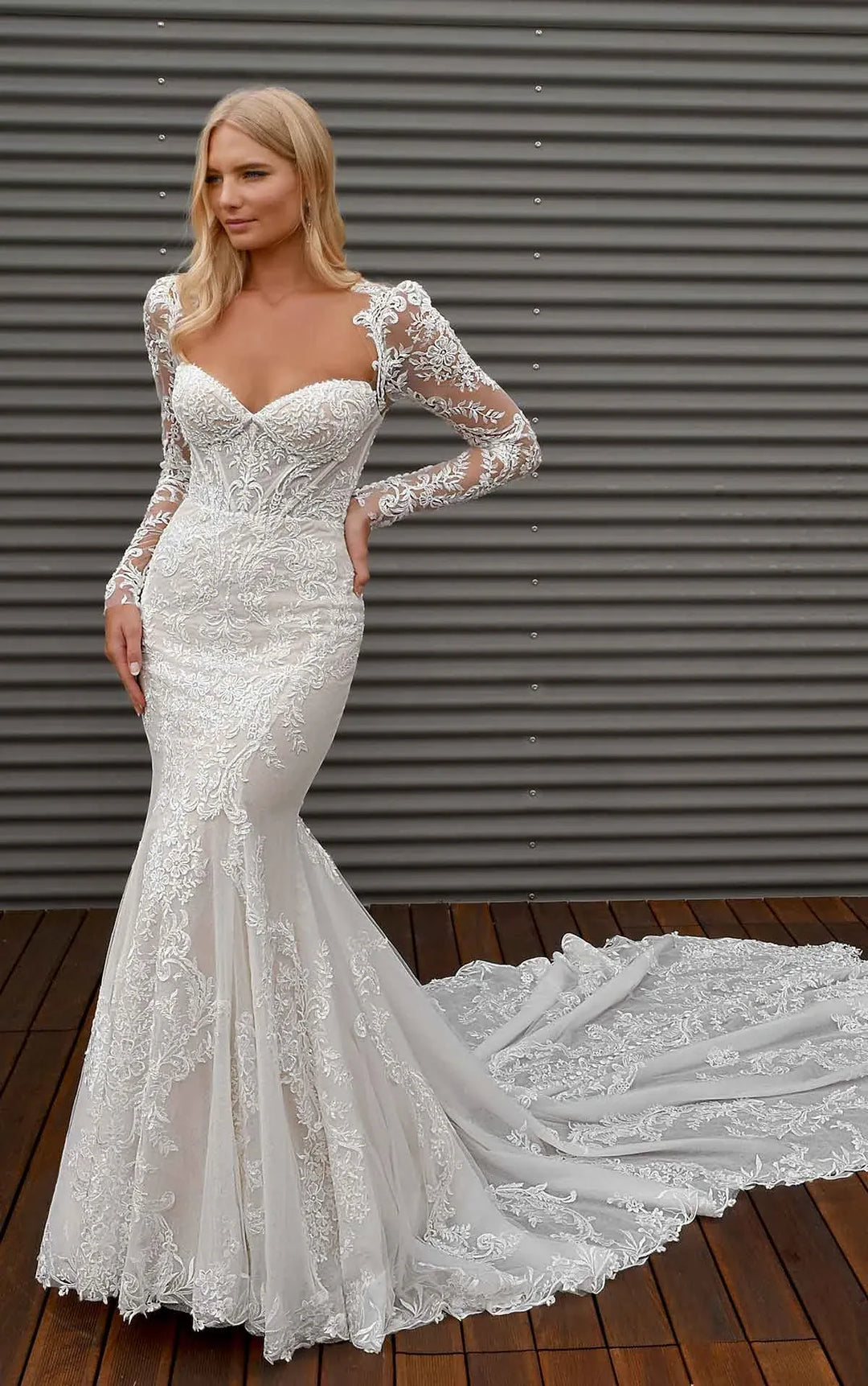 Woman wearing a white lace wedding dress with long sleeves against a metallic background.