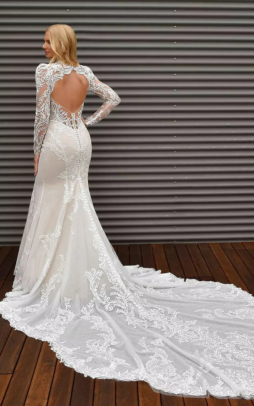 White lace wedding dress with long sleeves and open back on a wooden floor.