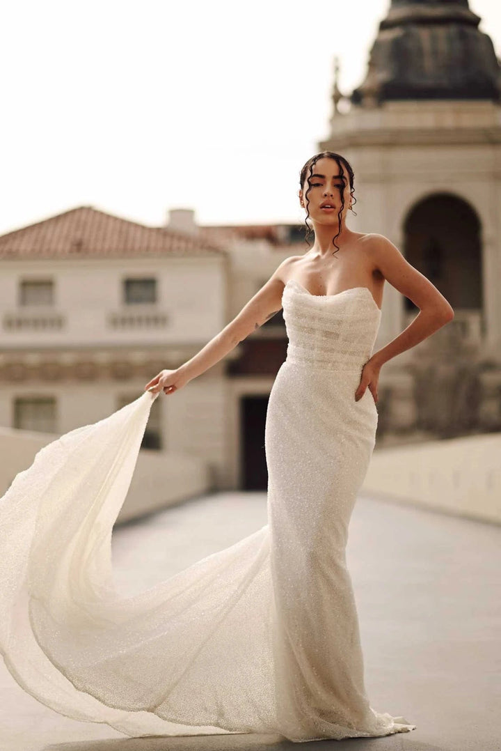 Woman in a white strapless gown with a flowing train standing in an urban setting.