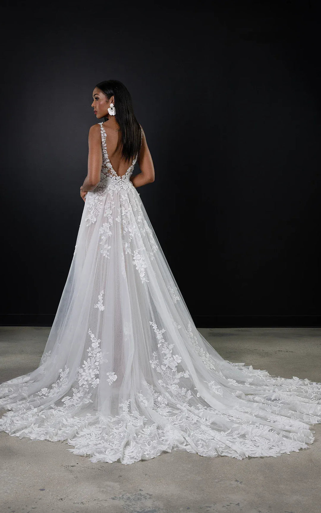Woman wearing a white lace wedding dress with a long train against a black background