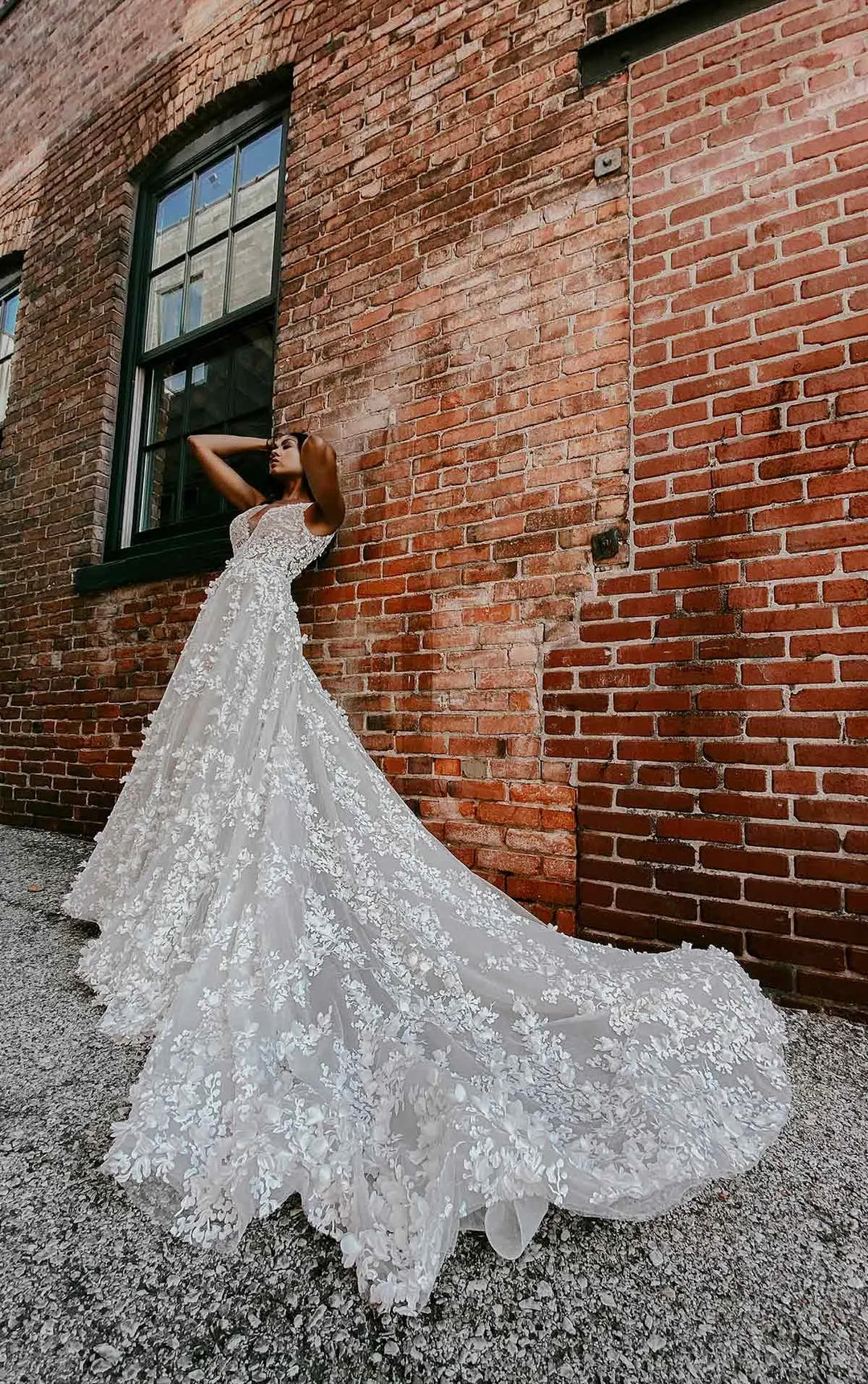 Woman in a white wedding dress standing against a brick wall.