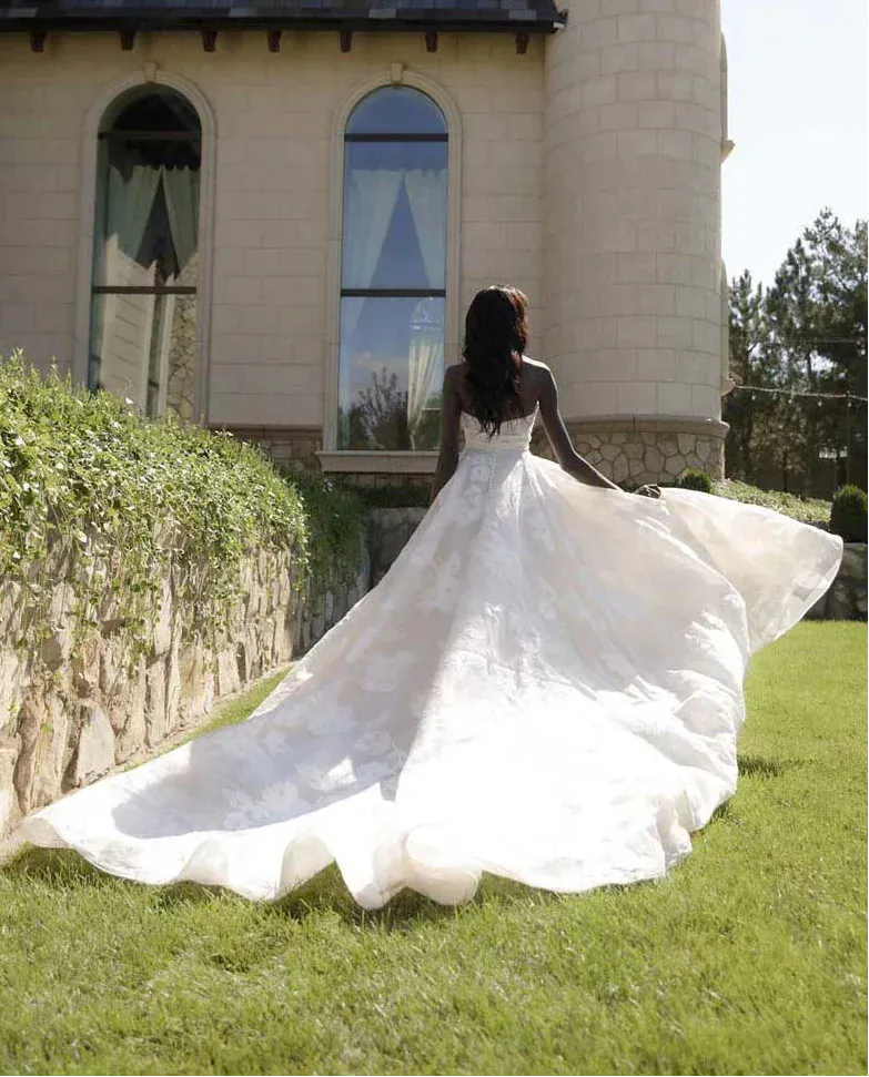 Woman in a white wedding dress standing in front of a stone building with a large stained glass window.