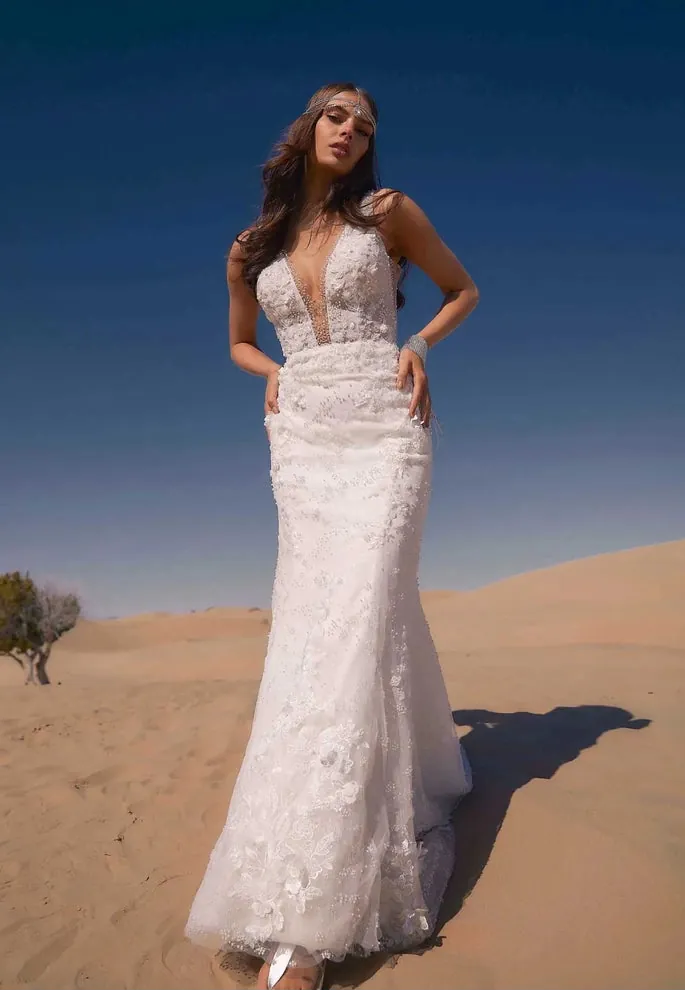 Woman in a white wedding dress standing in a desert landscape with a clear blue sky.