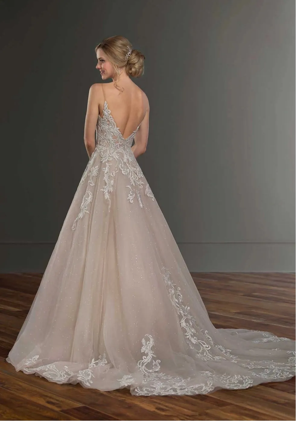 Woman wearing a lace wedding dress with a long train in a studio setting.